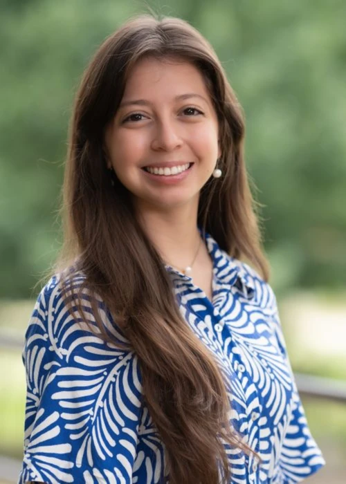 The image depicts a young women smiling in front of trees. 